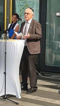 Bernd Krebs steht am Pult und spricht. Passanten hören zu